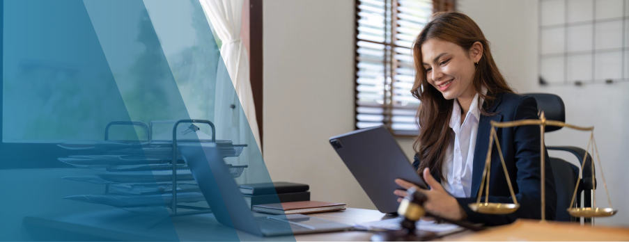 A woman dressed in a business suit is seated at a desk, working intently on her laptop in a professional environment.
