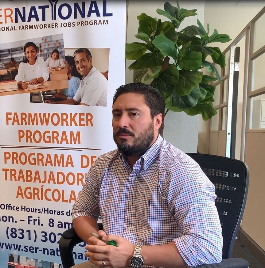 Man sitting in char next to a Farmworker Program Sign