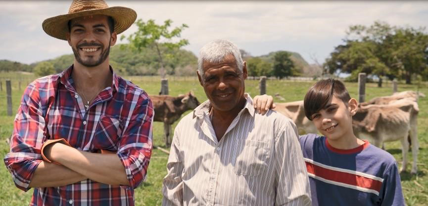 There are two men and a boy standing in a field with cows. 